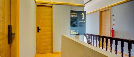 Un pasillo con una puerta de madera, un cartel que indica las habitaciones 301 a 308, y un extintor en la pared.