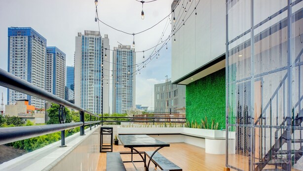 A modern rooftop terrace with a wooden floor, a black metal table, and a green wall. - Hotel O Alhesa Residence (Medan)