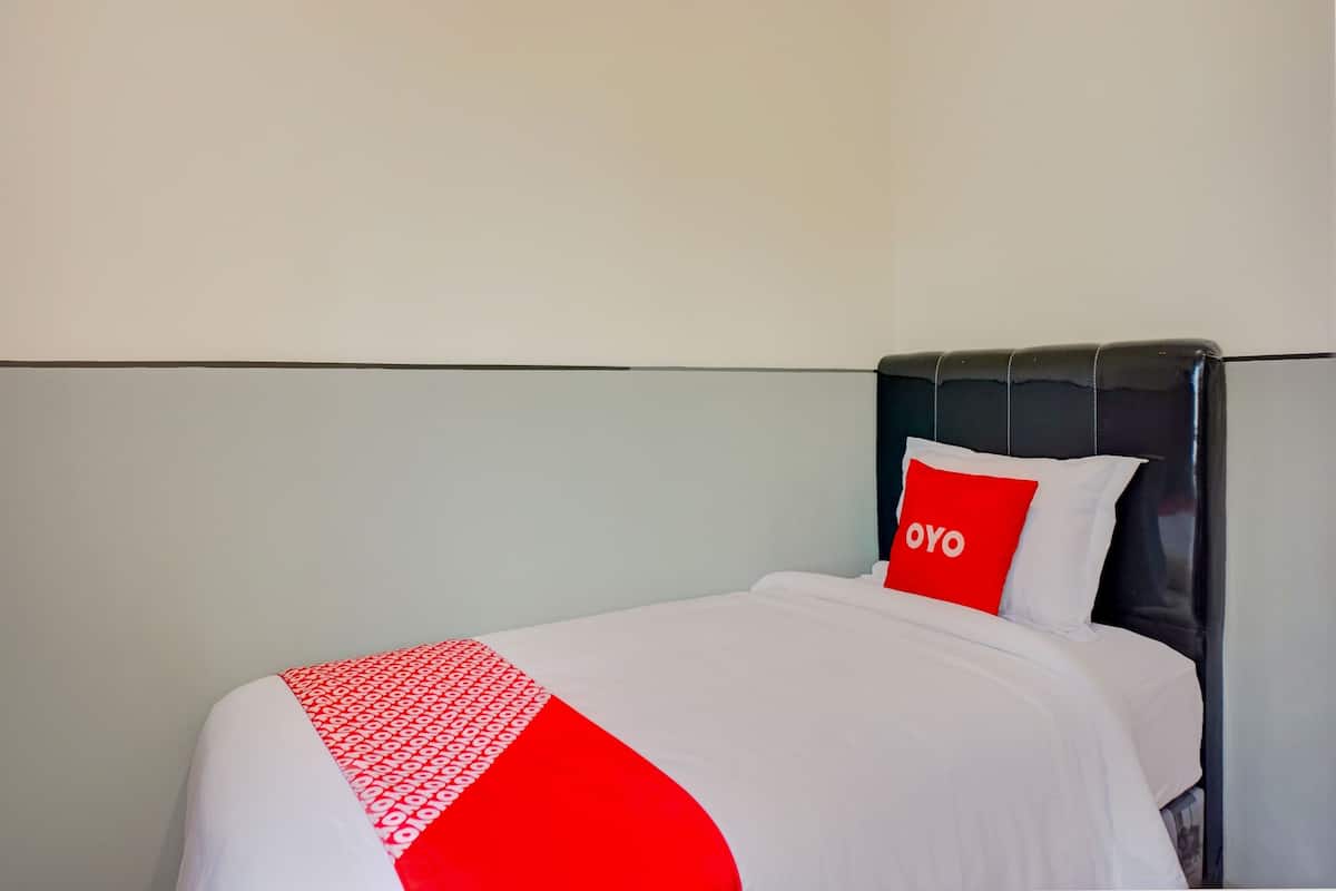 A hotel room with a bed, a red pillow with "OYO" text, and a white and red bedspread.
