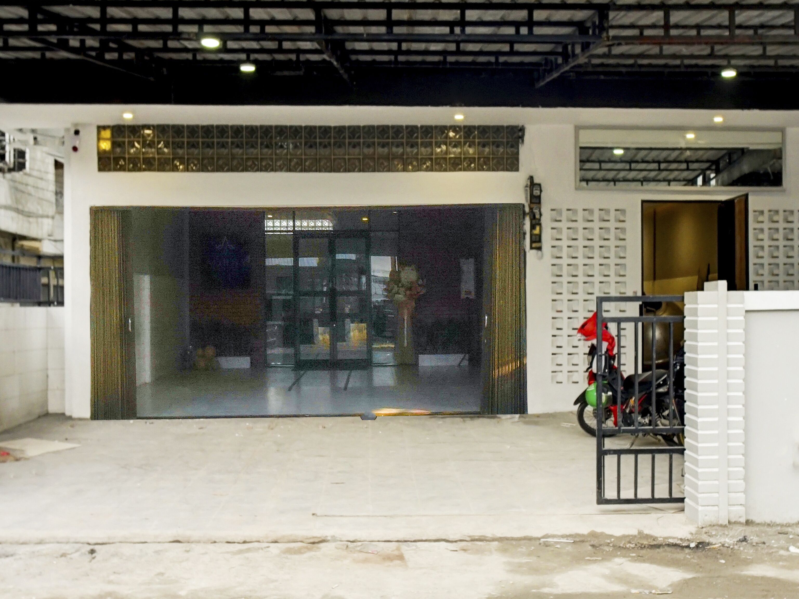 Una entrada de edificio con puerta de cristal, una motocicleta estacionada afuera y un muro de ladrillo.