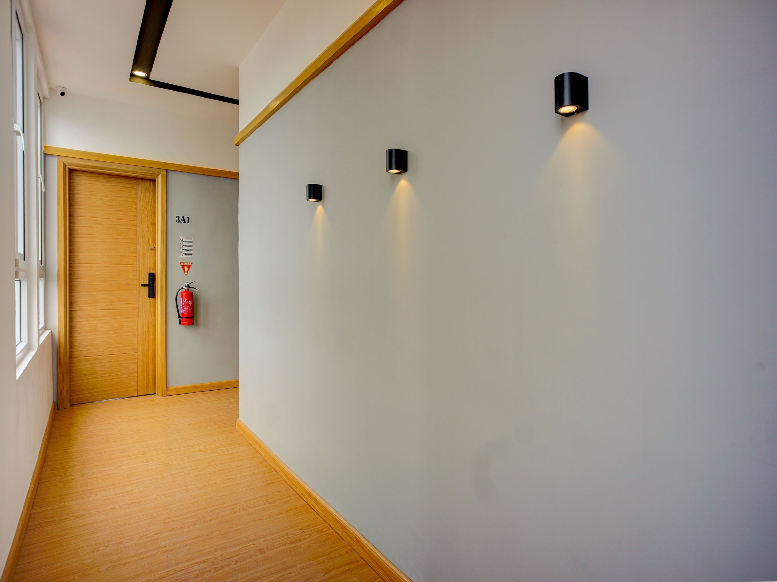 A hallway with wooden flooring, a wooden door, and three wall-mounted lights.