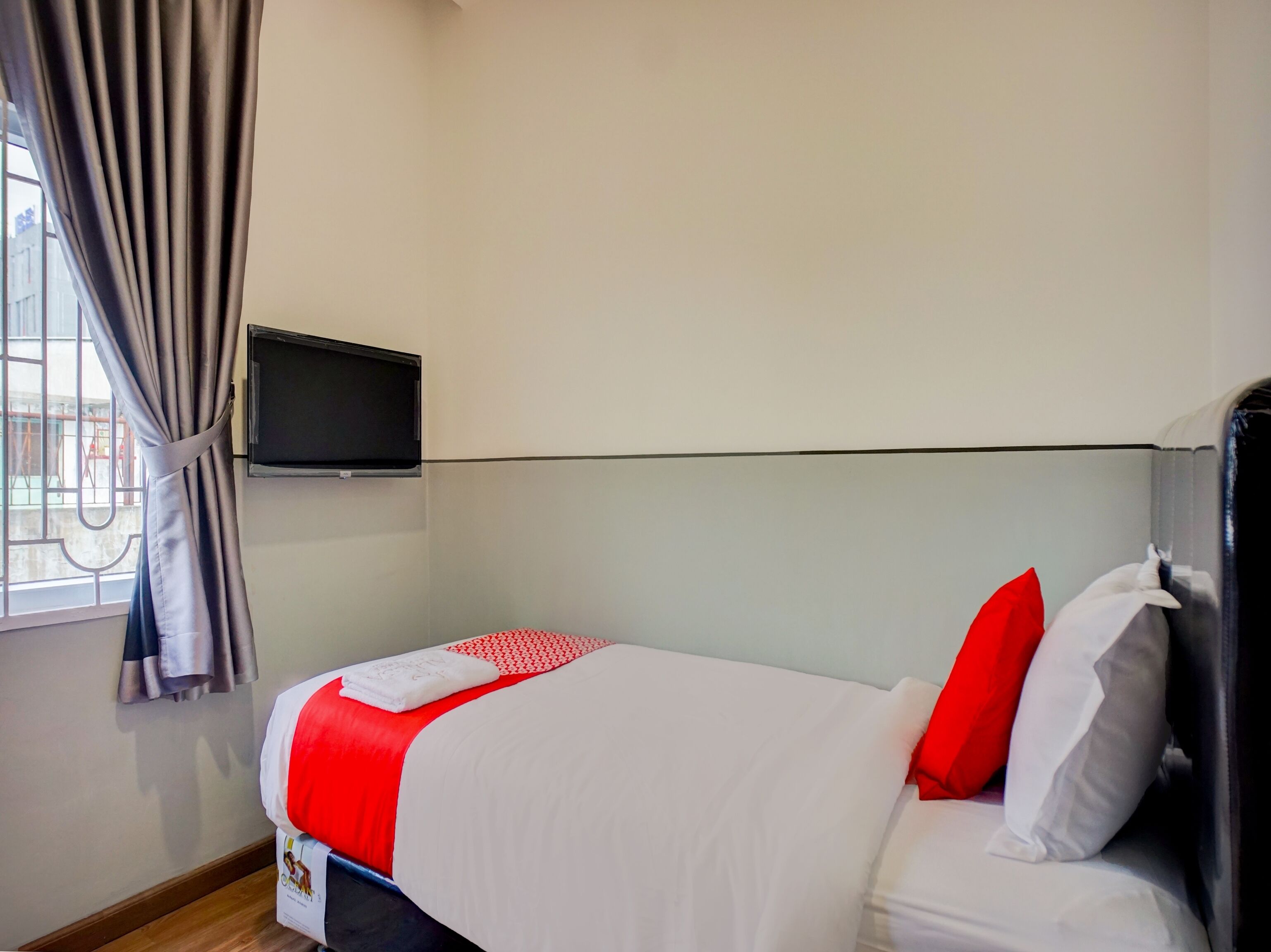 Una habitación de hotel con cama, televisor montado en la pared y ventana con cortinas.