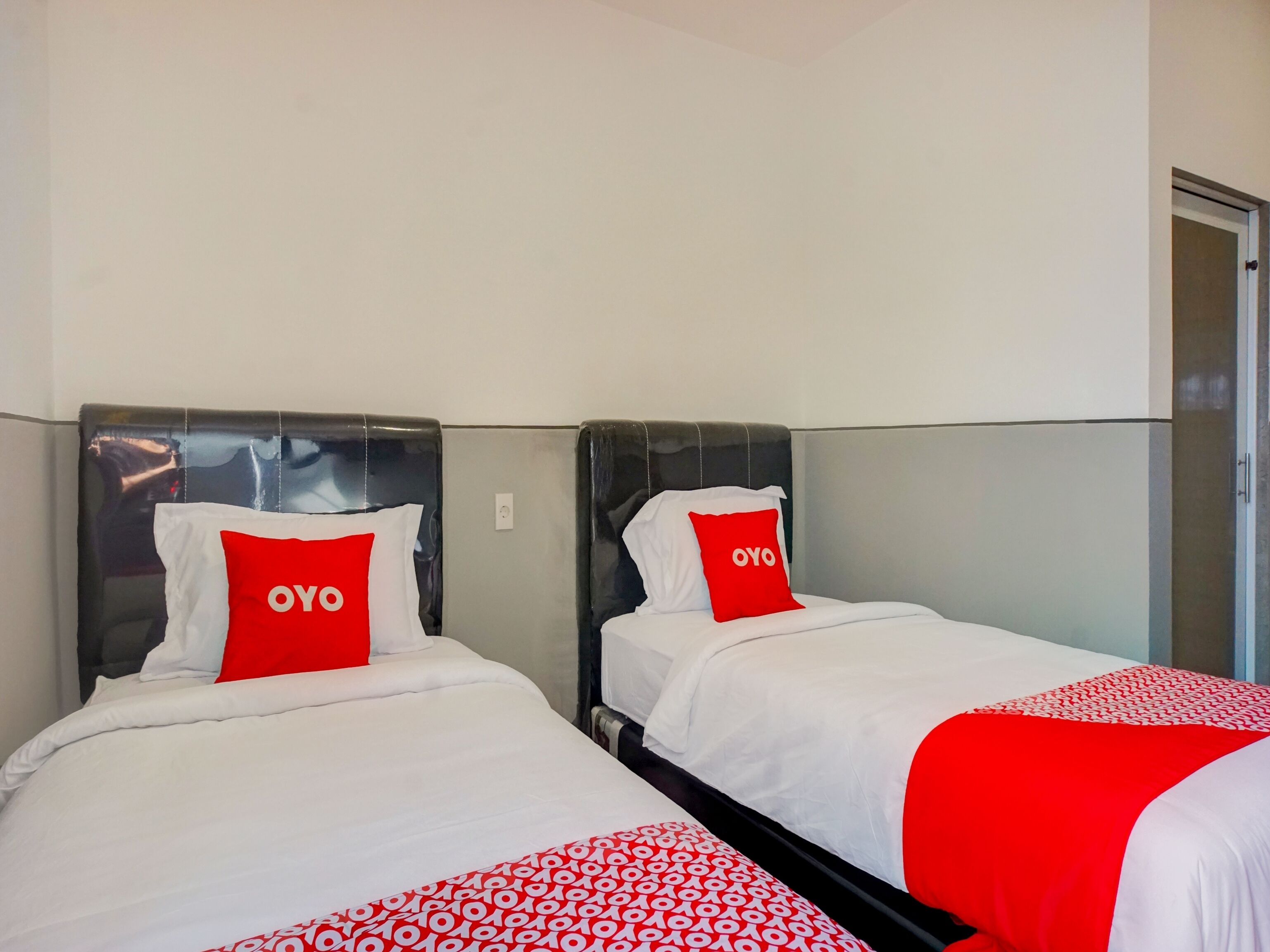 Dos camas con ropa blanca y almohadas rojas, cada una con la palabra 'OYO' escrita en ellas.