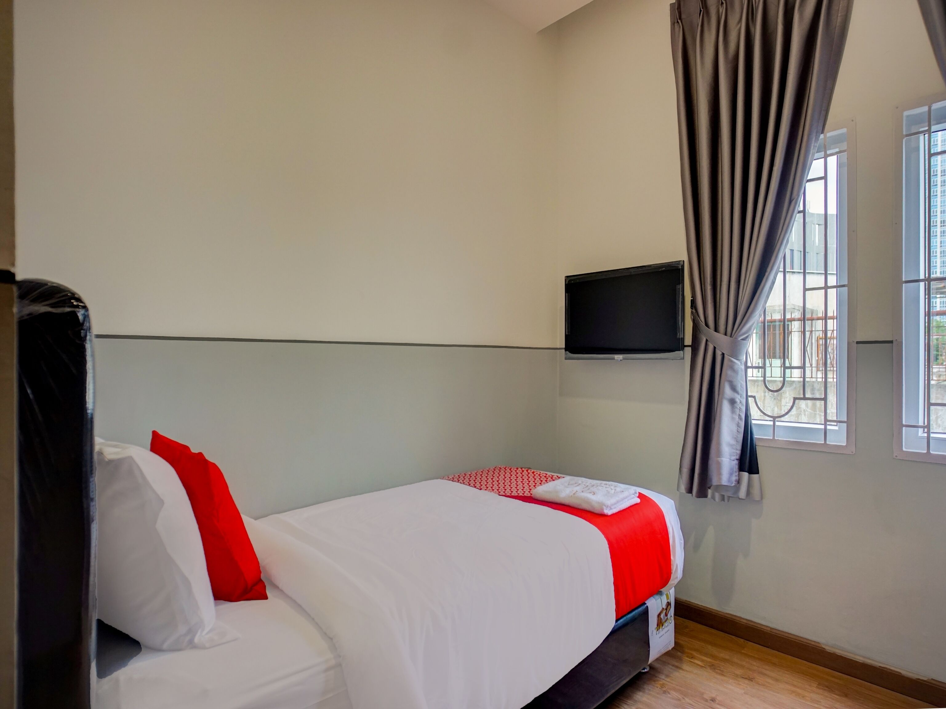 A hotel room with a single bed, a TV mounted on the wall, and a window with curtains.