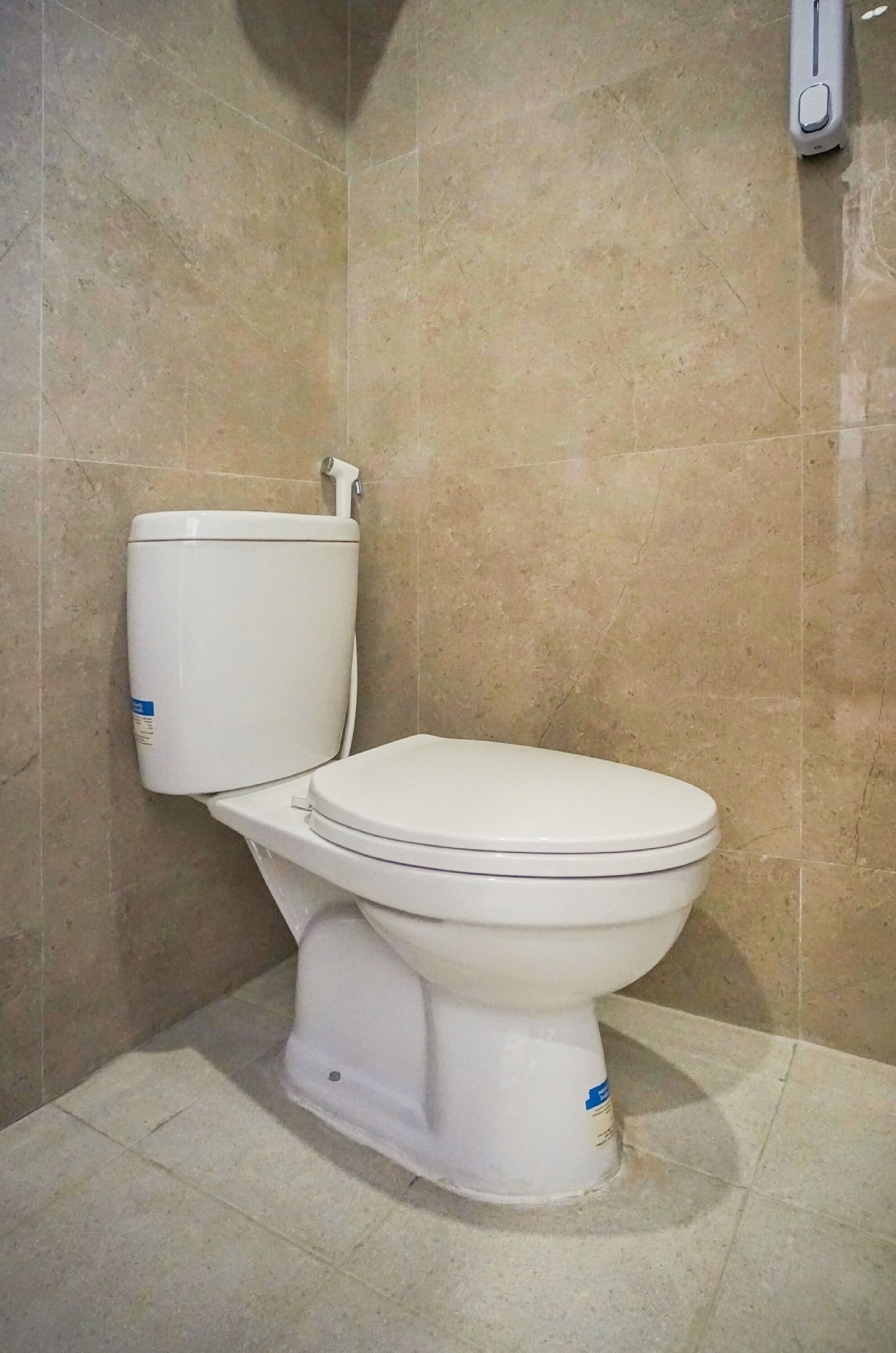 Een standaard toilet in een badkamer met beige tegels op de wanden en de vloer.