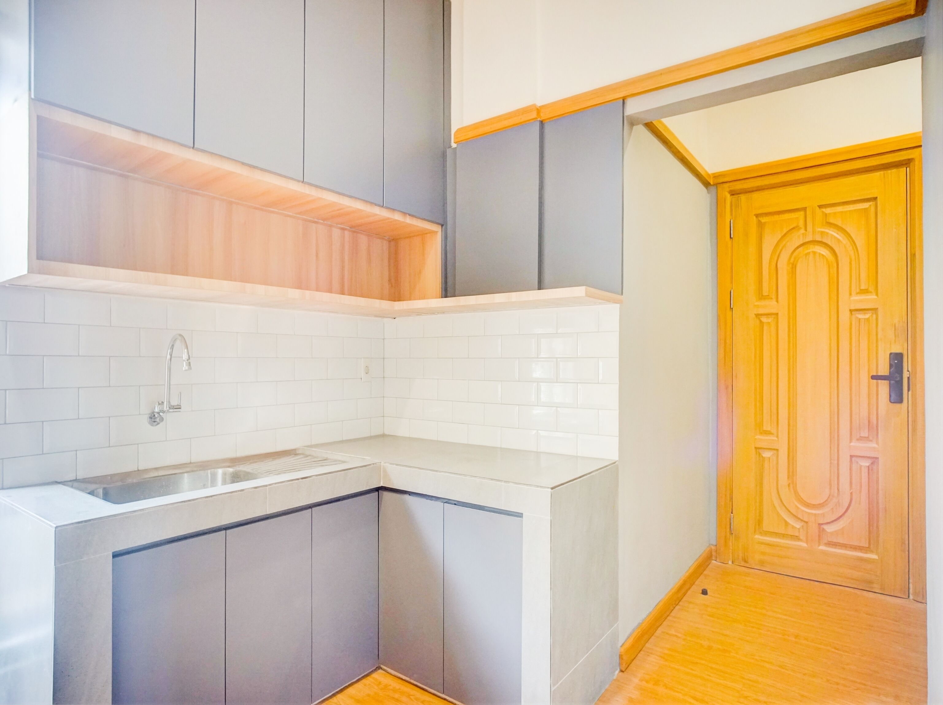 A modern kitchen with grey cabinets, white tiles, and a wooden door.