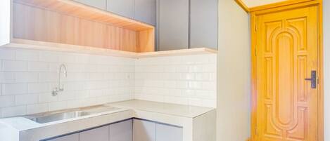 A modern kitchen with grey cabinets, white tiles, and a wooden door.