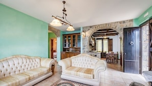 A spacious living room with two white sofas, a patterned rug, and a kitchen in the background.