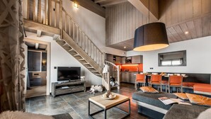 A spacious living area with a staircase, a television, a dining area with orange chairs, and a large pendant light. - Wifi, ski-in/ski-out & foot of the slopes, swimming pool, sauna, hammam, balcony, tv, ski locker (Val Thorens)