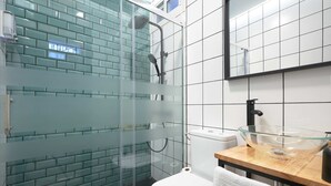 A modern bathroom with a glass shower enclosure, a white toilet, and a wooden vanity with a glass bowl sink. - Castilla 75, Urban Loft 1st floor (Sevilla)