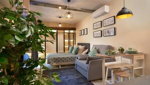 A modern bedroom with a bed, a desk, and a chair. There are plants, framed pictures on the wall, and an air conditioning unit. - Castilla 75, Urban Loft 1st floor (Sevilla)