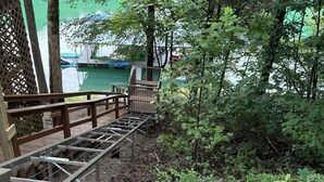 Une terrasse en bois avec une rambarde en métal, entourée d’une végétation luxuriante et offrant une vue sur un lac.