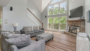 Un salon spacieux avec un plafond haut, une cheminée, une grande fenêtre et un escalier.
