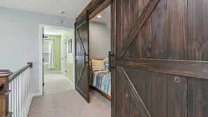 Une chambre avec une grande porte en bois, un lit recouvert d’une literie à motifs et un sol recouvert d’une moquette.