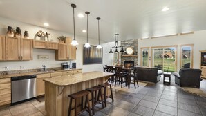 A spacious kitchen with wooden cabinets, a granite countertop, and a built-in dishwasher. There is a dining area with a stone fireplace and a view of the outdoors. - Overlooks 9th Green | Discount Golf Privileges | Golf & Ski (South Fork)