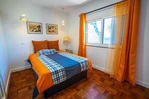 Quarto com cama, duas mesas de cabeceira, janela com cortinas e duas luminárias fixadas na parede.