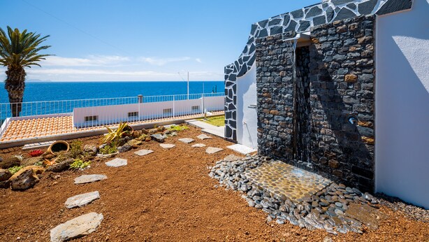 Un bâtiment situé sur la côte, doté d’une façade en pierre, d’un petit élément décoratif aquatique et offrant une vue sur la mer.