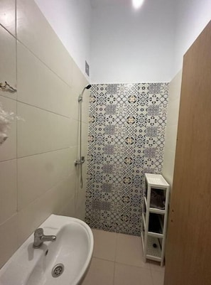 Un baño pequeño con lavamanos, ducha y repisa con artículos de tocador.