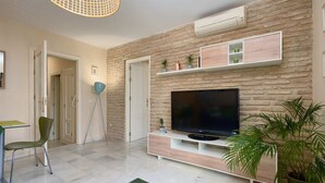 A modern living room with a flat-screen TV, a stone wall, a white entertainment unit, a floor lamp, and a green chair. - Castilla 75, Apartment 2 bedrooms 2nd Floor (Sevilla)