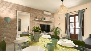 A dining area with a brick wall, a television, and a window with curtains. - Castilla 75, Apartment 2 bedrooms 2nd Floor (Sevilla)