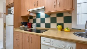 A compact kitchen with wooden cabinets, a built-in microwave, a dishwasher, and a checkered backsplash. - Castilla 75, Apartment 2 bedrooms 2nd Floor (Sevilla)