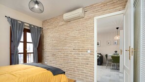 A bedroom with a brick wall, a bed with a yellow bedspread, grey curtains, and an air conditioning unit. - Castilla 75, Apartment 2 bedrooms 2nd Floor (Sevilla)