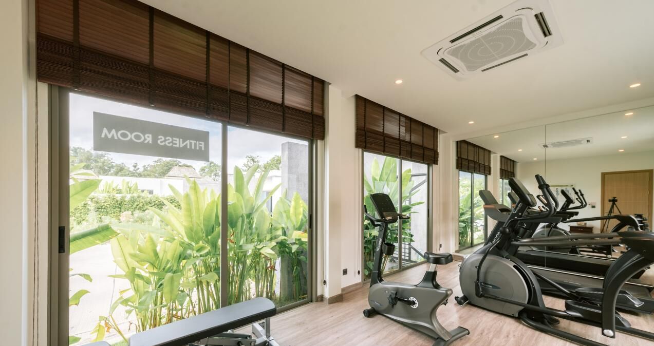A fitness room with exercise equipment, large windows, and a view of greenery.