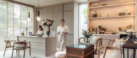 Un moderno vestíbulo de hotel con mostrador de recepción, área de descanso y una cocina visible al fondo.