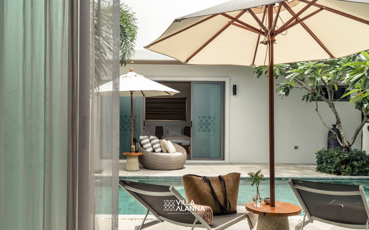 Un área junto a la piscina con sillones de descanso, una silla de mimbre y una sombrilla grande.