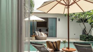 Un área junto a la piscina con sillones de descanso, una silla de mimbre y una sombrilla grande.