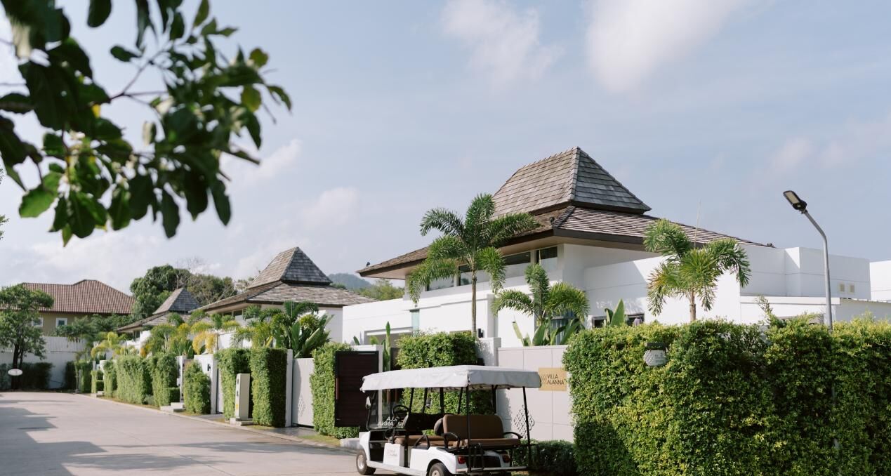 A row of modern villas with sloped roofs, surrounded by well-maintained hedges and palm trees.