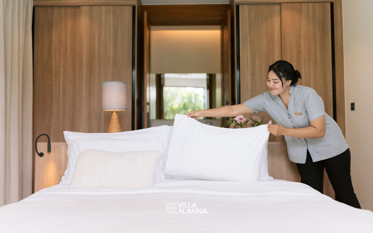 A hotel room with a neatly made bed, a bedside lamp, and a view of the outdoors through a sliding door.