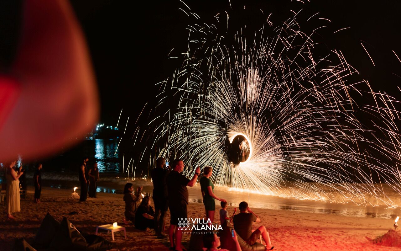 A beach scene with people gathered around a firework display.