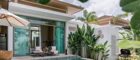A modern villa with a swimming pool, outdoor seating, and lush greenery.