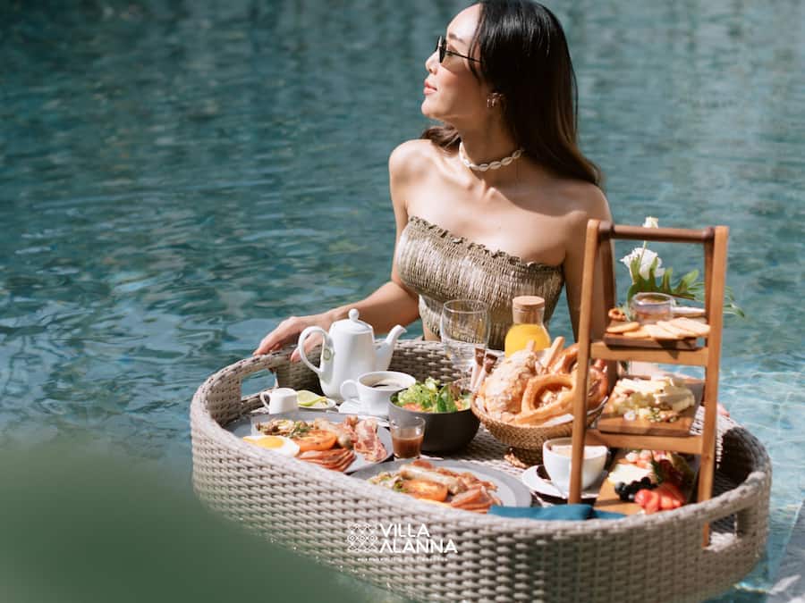 Una persona sentada junto a una mesa en la piscina, con una cesta que contiene comida y bebidas.