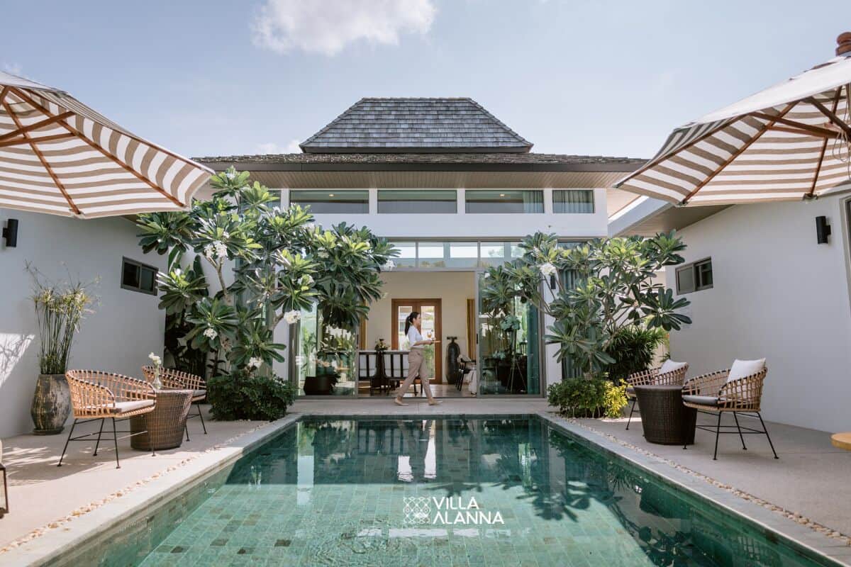A pool area with lounge chairs and umbrellas, surrounded by lush greenery and a modern building.