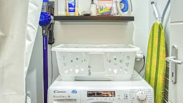 Un área de lavandería compacta con lavadora de carga frontal, un tendedero y un estante con productos de limpieza.