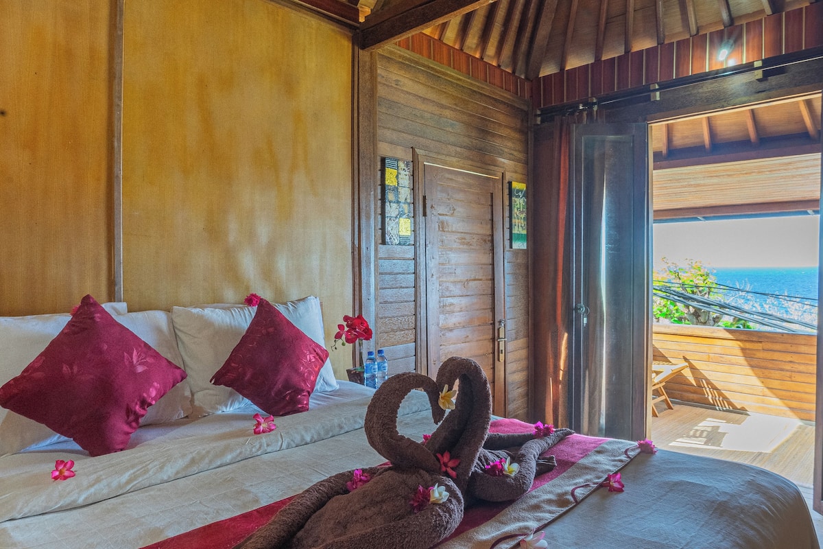 A bed with a heart-shaped towel arrangement, a wooden ceiling, and a view of the outdoors.
