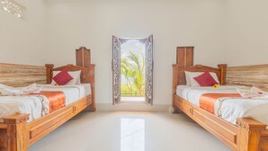 Ein Zimmer mit zwei hölzernen Betten, weißer Bettwäsche und Blick auf Palmen durch einen verzierten Durchgang.