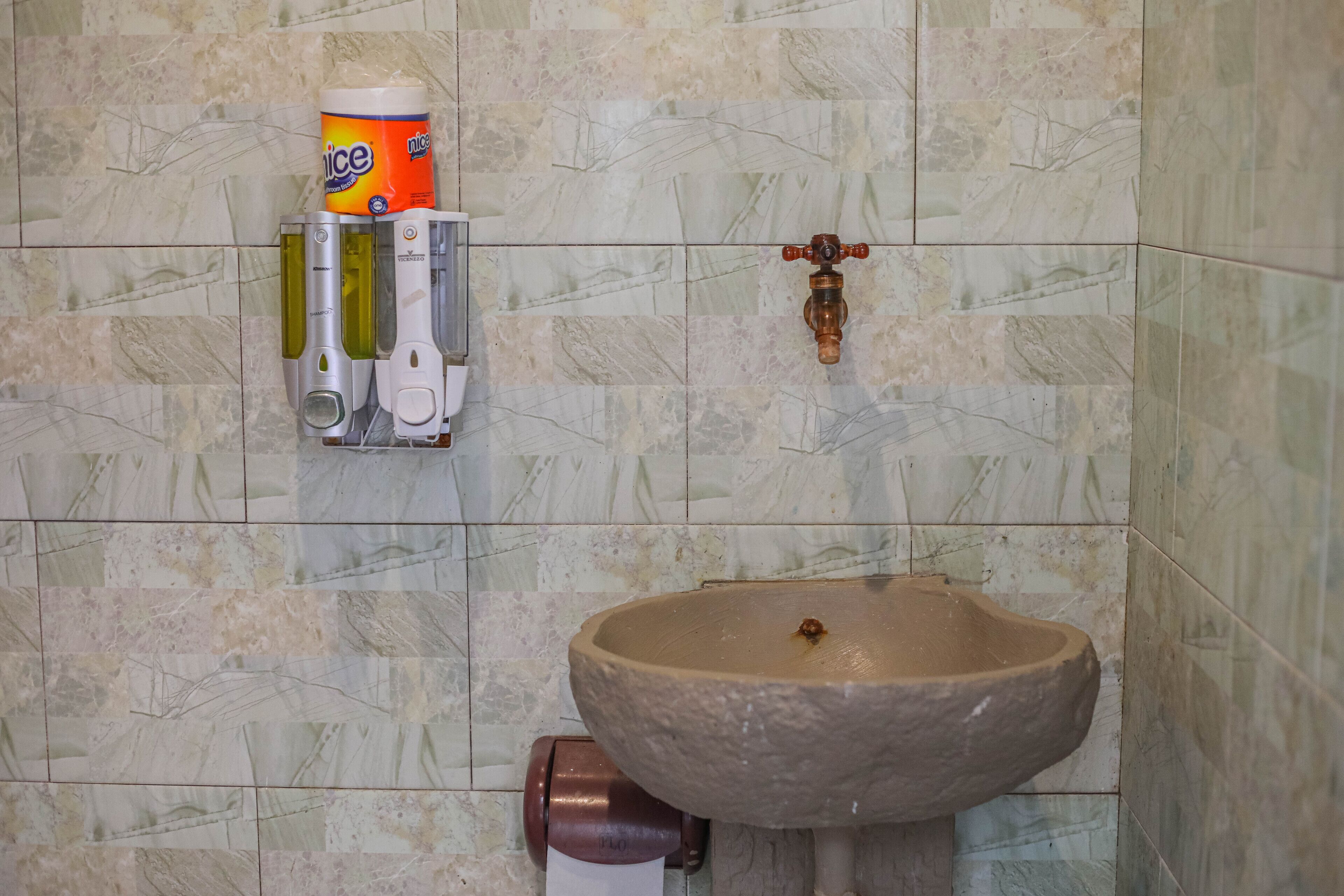 A bathroom with a stone sink, a hand soap dispenser, and a paper towel dispenser.