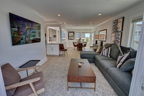 A modern living room with a grey sofa, a coffee table, and a dining area in the background. - Springbreak Getaway 3BD/2BA, garage,2Bikes A View (newport beach)