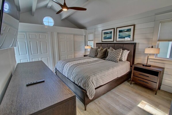 A bedroom with a bed, bedside tables, a desk, a ceiling fan, and two framed pictures on the wall.