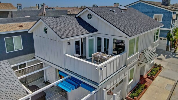 Ein zweistöckiges Haus mit Balkon, überdachter Terrasse und kleinem Garten.
