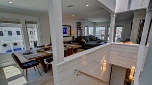 Ein modernes Wohnzimmer mit Essbereich, großen Fenstern und einer Treppe, die zu einer oberen Etage führt.