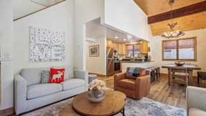 A spacious living area with a grey sofa, a round wooden coffee table, and a dining area with a wooden table and chairs.