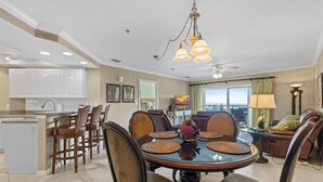 A spacious kitchen with white cabinets, a dining area with a round table and chairs, and a living room with a sofa and a TV.