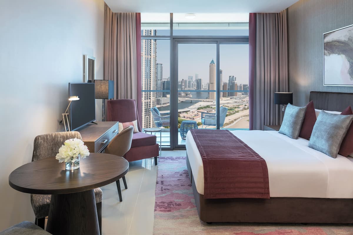 Ein modernes Hotelzimmer mit einem großen Bett, einem Schreibtisch, einem Stuhl und Blick auf die Stadt.