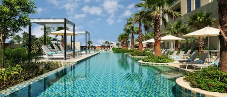 A swimming pool with lounge chairs and umbrellas, surrounded by palm trees and a building.