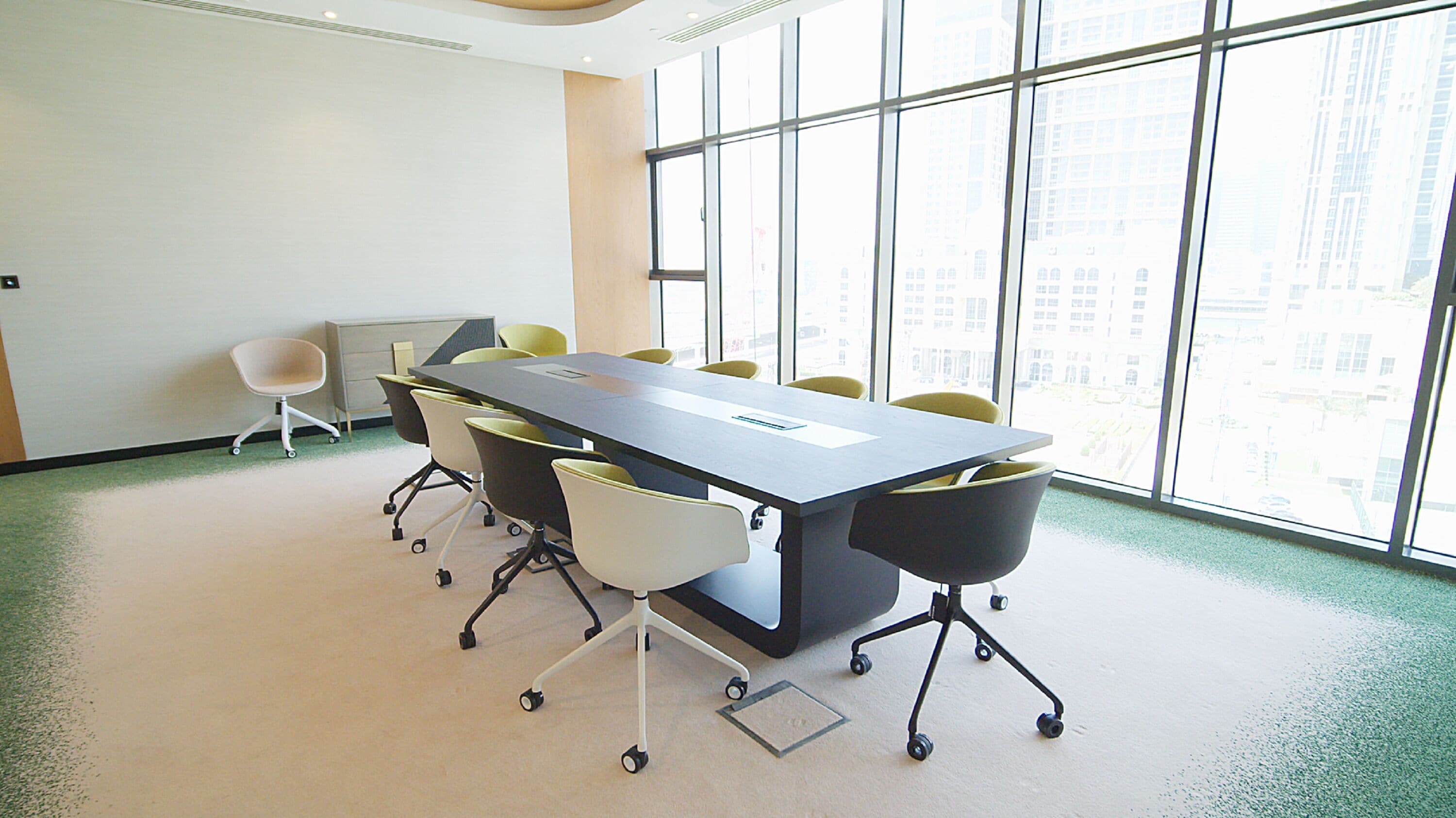 A conference room with a large table, six chairs, and a view of a cityscape through large windows.