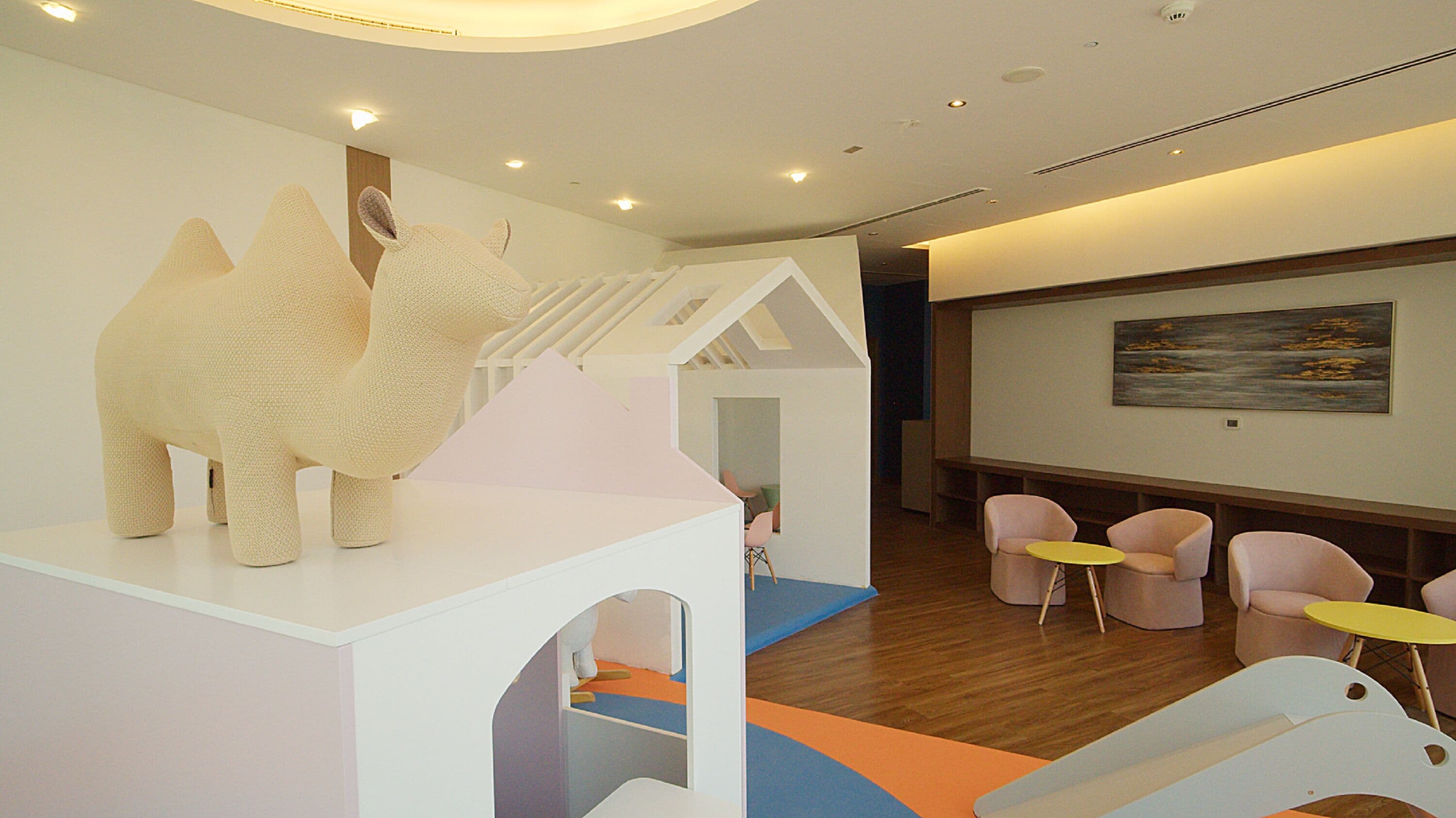 A modern interior with a white play area, a staircase, and a seating area with tables and chairs.